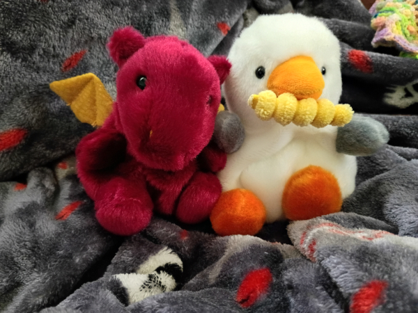 A dragon and seagull palm pal. The dragon is ruby red with golden yellow wings. The seagull has a plush french fry in its mouth.